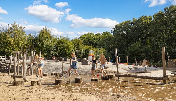 Kids jumping over logs and water in playground at Het Genieten